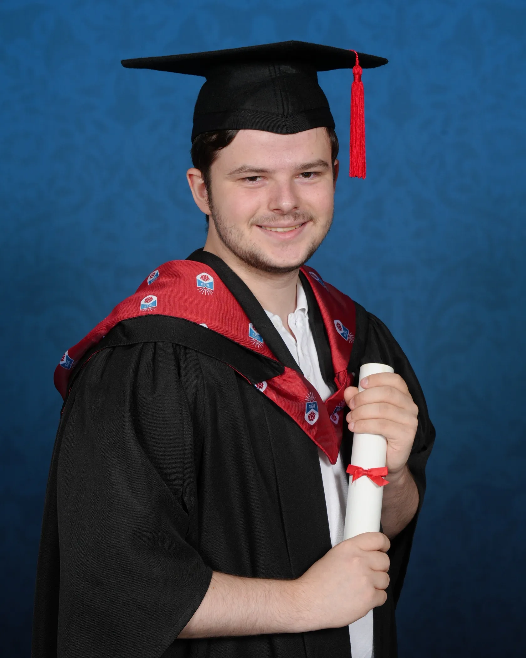 Owen Bladen-Kay smiling in his graduation cap and gown, holding his degree scroll.