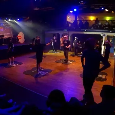 Players competing in VR on the floor, with Duckman cutouts at the edge of the stage.