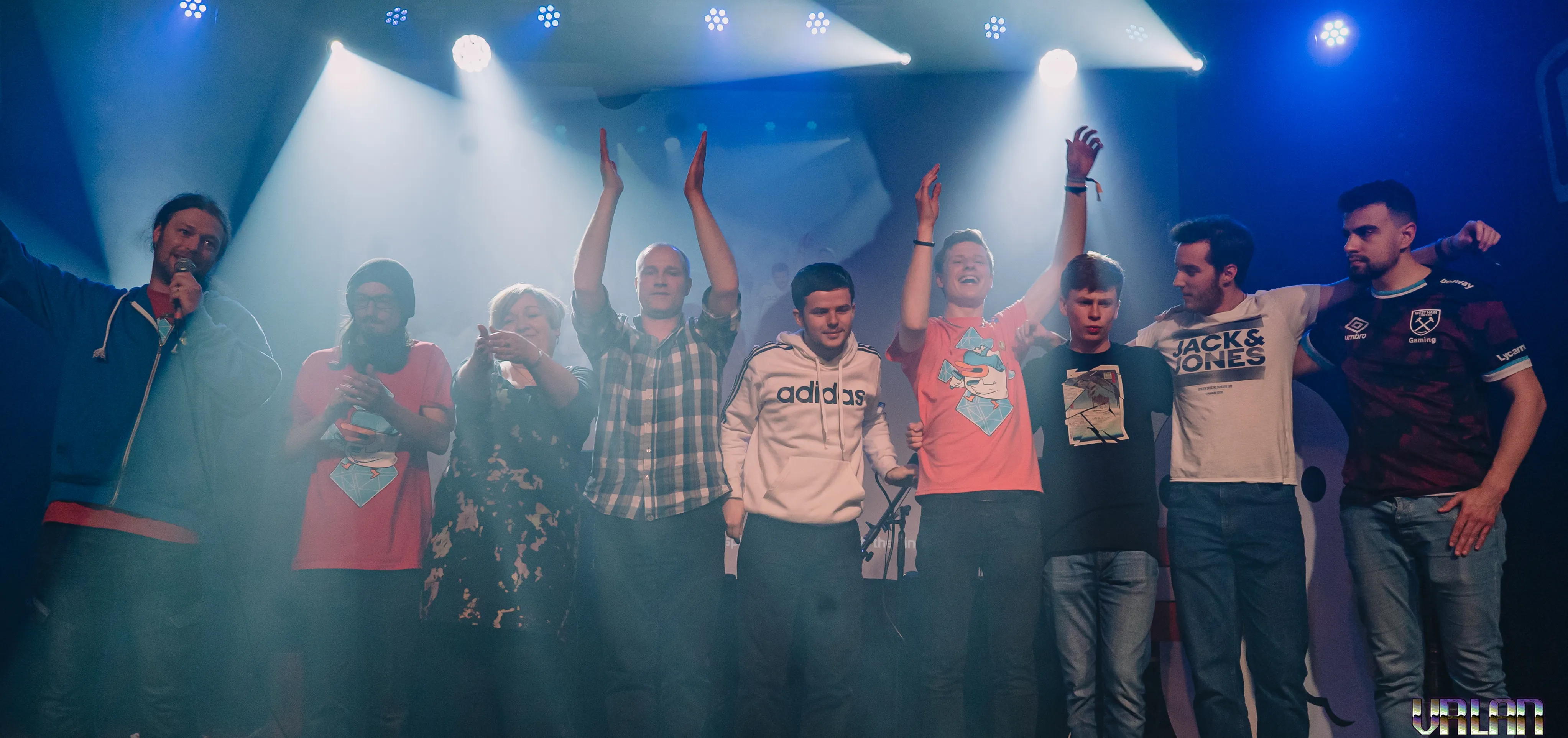 A team celebrating on stage with their arms in the air.