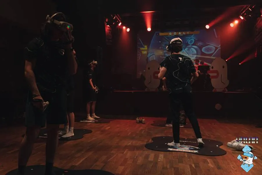 Players in headsets on play mats in front of the stage screen.